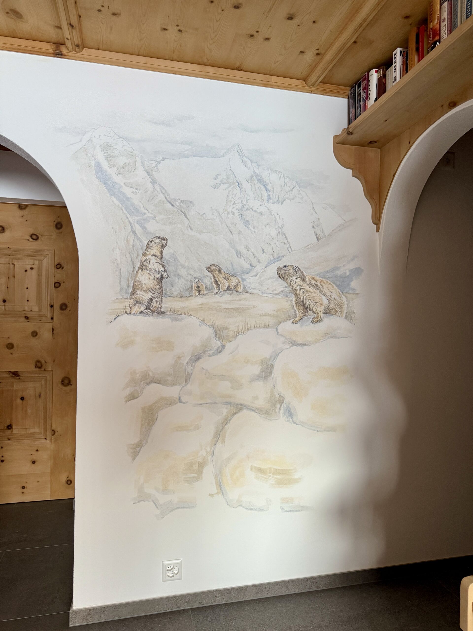 Wandbild mit Murmeltieren in Alpenlandschaft auf weißer Wand. Handgemalte Naturkunst für gemütliches Zuhause.
